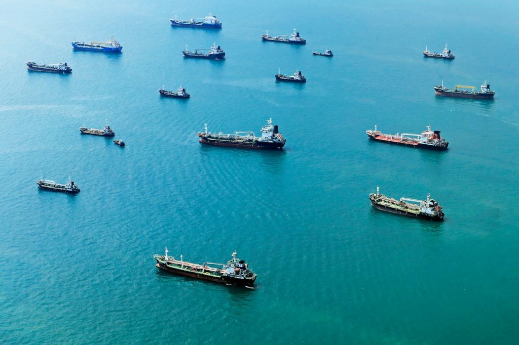 pexels-photo-35421778 Numerous cargo ships anchored on the blue ocean, captured from above.